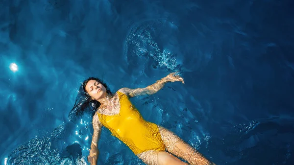 Jeune femme en maillot de bain une pièce jaune flotte à la surface de l'eau . — Photo