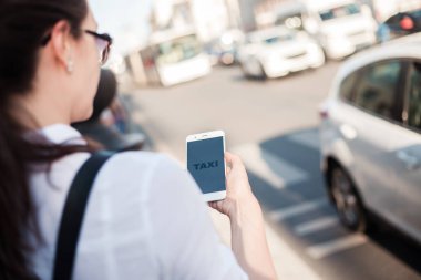 Mobil uygulamayı kullanarak taksi çağırın. Şehirde genç bir kadın elinde bir akıllı telefon ile yolun yanında duruyor