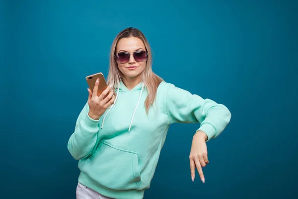 Elegante moderno hipster menina com capuz azul com o capuz usa um smartphone. — Fotografia de Stock