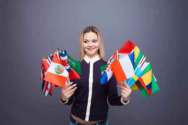 Vrolijke jonge vrouw met een groot aantal vlaggen van verschillende landen van de wereld — Stockfoto