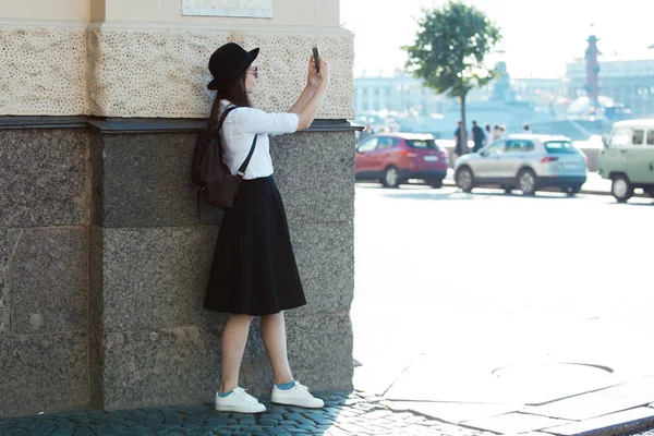 Touristen in der Stadt machen ein Foto mit dem Smartphone. eine junge Frau mit schwarzem Hut und weißem Hemd, — Stockfoto