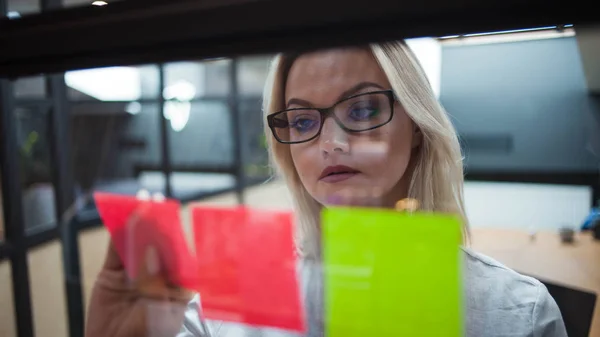 Молодая женщина в офисе клеит липкие простыни на стеклянном перегородке офиса . — стоковое фото
