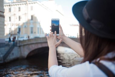 Şehirde turist Smartphone bir fotoğraf çeker. Siyah şapkalı genç bir kadın ve beyaz bir gömlek,