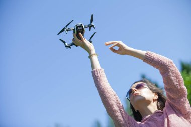 Parkta genç bir kadın başlattı, başka bir kontrol panelinde, başının üzerinde onu uzanmış kolu ile drone tutar.