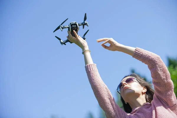 Una joven en el parque lanza, sostiene el dron con su brazo extendido por encima de su cabeza, en otro panel de control . —  Fotos de Stock