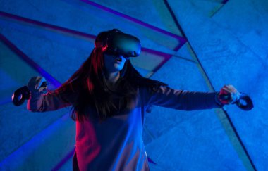 Kılıç kullan. Sanal kasklı genç bir kadın, sanal kılıçların kolları gibi her iki elinde de kontrolörler kullanır..