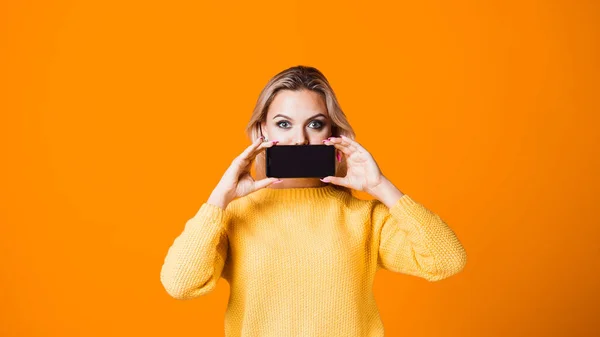 Mulher jovem bonito em uma camisola amarela segurando um smartphone — Fotografia de Stock