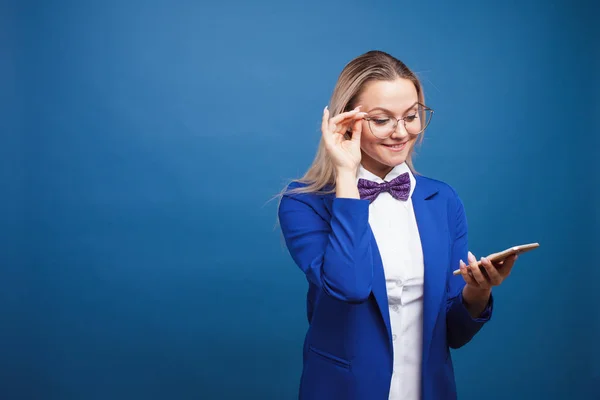 Leuke en grappige zakenvrouw in een stijlvolle blauwe jas en strikje maakt gebruik van een smartphone. — Stockfoto