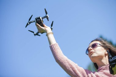 Parkta genç bir kadın başlattı, başka bir kontrol panelinde, başının üzerinde onu uzanmış kolu ile drone tutar.