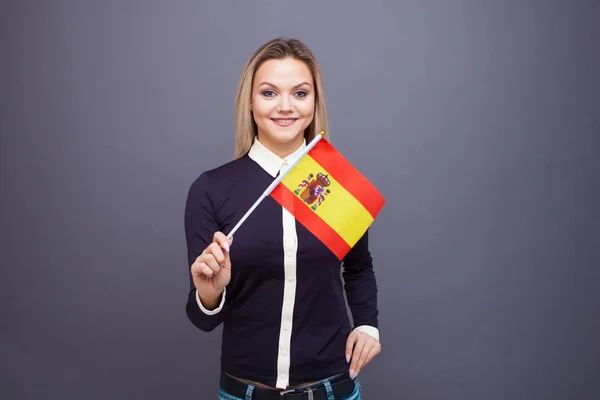 Μετανάστευση και μελέτη ξένων γλωσσών, έννοια. Μια νεαρή χαμογελαστή γυναίκα με μια ισπανική σημαία στο χέρι της. — Φωτογραφία Αρχείου