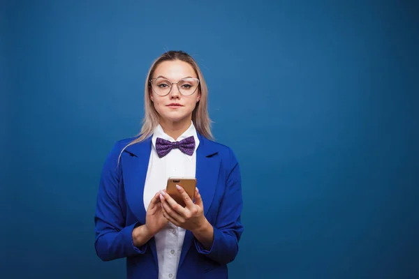 Mujer de negocios linda y divertida en una elegante chaqueta azul y pajarita utiliza un teléfono inteligente . — Foto de Stock