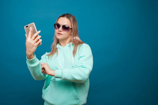 Loura alegre com um telefone celular. Retrato de uma jovem mulher positiva com capuz azul — Fotografia de Stock