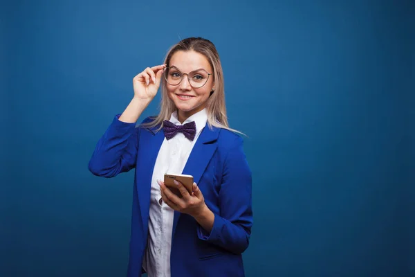 Leuke en grappige zakenvrouw in een stijlvolle blauwe jas en strikje maakt gebruik van een smartphone. — Stockfoto