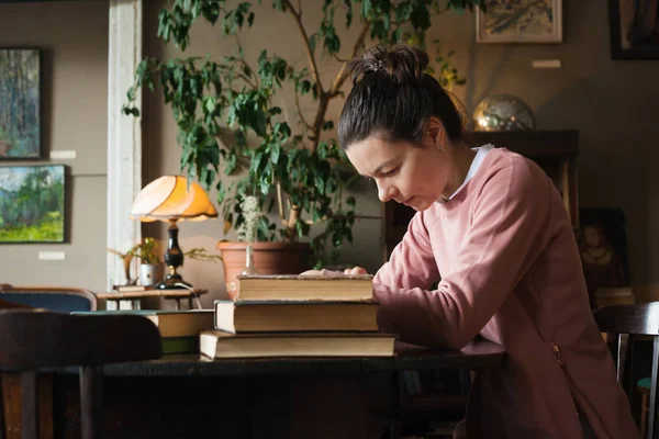 Voorbereiding van het examen. Student meisje in glazen en een roze trui die over boeken, bezig met een oude bibliotheek aan de tafel. — Stockfoto