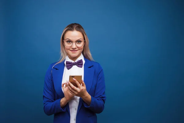 Cute i zabawne businesswoman w stylowej niebieskiej kurtce i muszki używa smartfona. — Zdjęcie stockowe