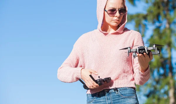 Una joven con capucha rosa y gafas oscuras sostiene el dron con una mano, y sostiene el panel de control en la otra . —  Fotos de Stock