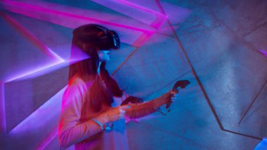 Sanal gerçeklik gözlük genç bir kadın neon süslemeleri ile duvar arka plan karşı, denetleyicileri kullanır.