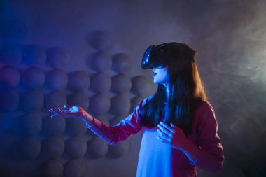 Sanal gerçeklik gözlüklerinde şaşırmış bir kadın havaya dokunur, bir şey bulmaya çalışır, görünmez bir kontrol paneli kullanır.