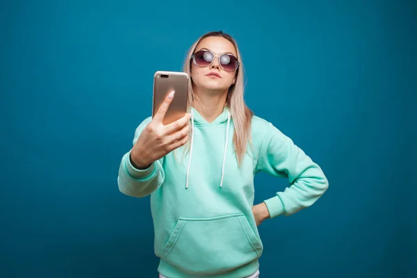 Loura alegre com um telefone celular. Retrato de uma jovem mulher positiva com capuz azul — Fotografia de Stock