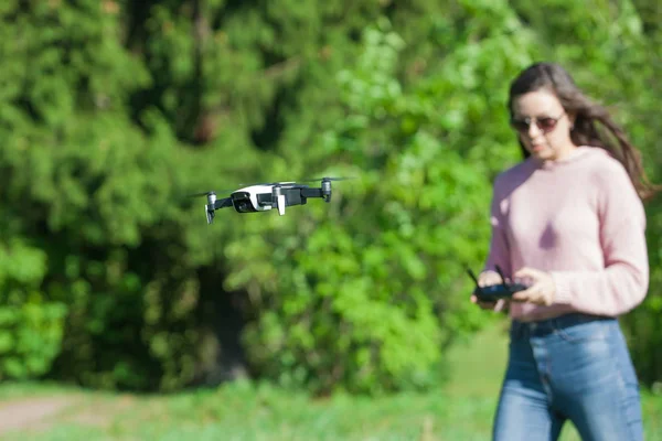 Giovane donna che indossa occhiali da sole e cappuccio sulla testa tenendo un telecomando, guarda attentamente in lontananza contro . — Foto Stock