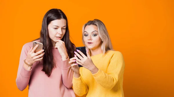Bionda e bruna con i loro smartphone su uno sfondo giallo brillante . — Foto Stock