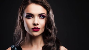Portrait of a young luxurious woman in a low key. Bright makeup with scarlet lipstick, hairstyle with curls,