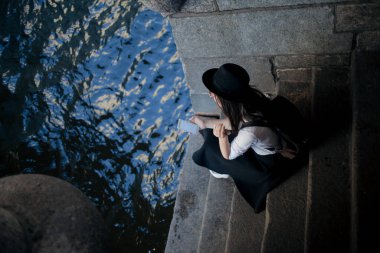 bir şapkalı genç kadın ve bir sırt çantası ile şehirde yürür ve bir akıllı telefon kullanır.