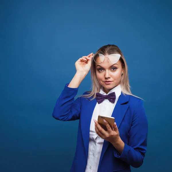 Mujer de negocios linda y divertida en una elegante chaqueta azul y pajarita utiliza un teléfono inteligente . — Foto de Stock