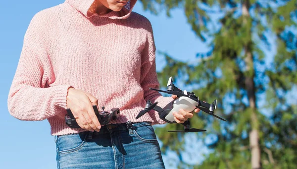 Una giovane donna con una felpa rosa e occhiali scuri tiene drone con una mano, e tiene il pannello di controllo nell'altra . — Foto Stock
