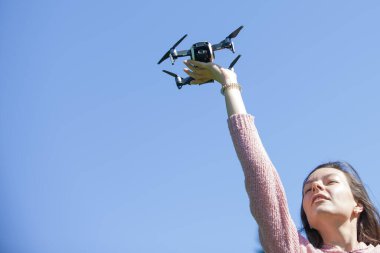Parkta genç bir kadın başlattı, başka bir kontrol panelinde, başının üzerinde onu uzanmış kolu ile drone tutar.