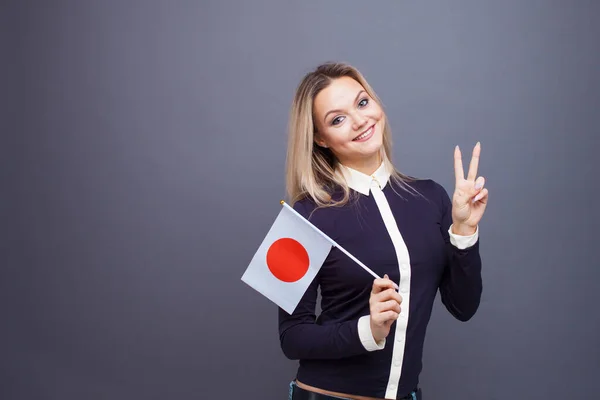 Imigrace a studium cizích jazyků, koncepce. Mladá usměvavá žena s japonskou vlajkou v ruce. — Stock fotografie