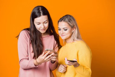 Sarışın ve esmer, parlak sarı arka planda akıllı telefonları var..