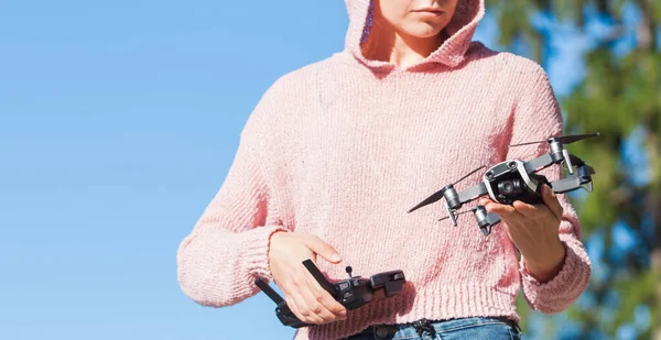 Una giovane donna con una felpa rosa e occhiali scuri tiene drone con una mano, e tiene il pannello di controllo nell'altra . — Foto Stock