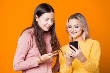 Sarışın ve esmer, parlak sarı arka planda akıllı telefonları var..