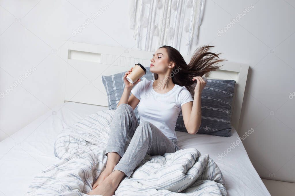 Wake up in bed in the morning and drink coffee. Young beautiful girl sitting on the bed