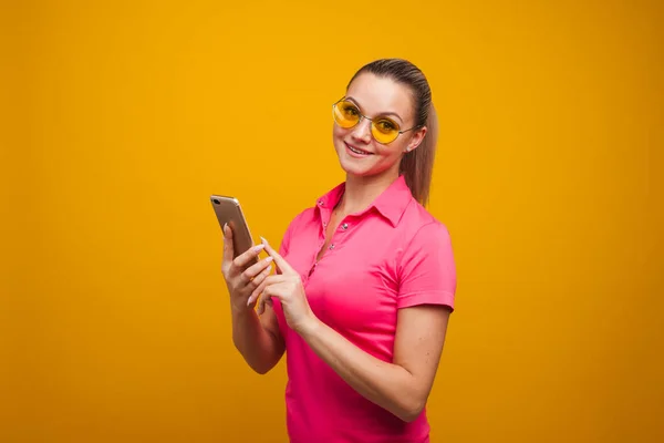 Bright and positive young woman with smartphone on yellow background. The girl uses a smartphone