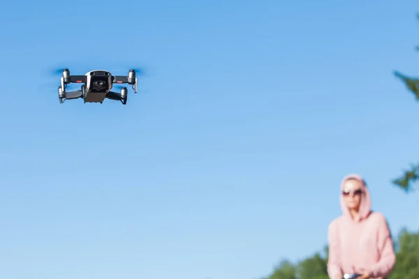 Mujer joven con capucha rosa y gafas oscuras controla el panel de control de vuelo del dron . —  Fotos de Stock