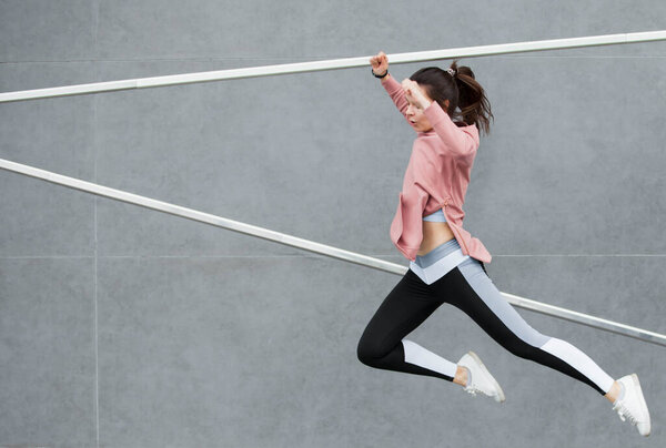 An athletic young woman is jumping, doing acrobatics, ballet, is actively involved in sports, against a concrete wall.