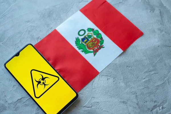 Situação epidemiológica no país Peru. Bandeira e smartphone com notícias e um símbolo de risco biológico . — Fotografia de Stock