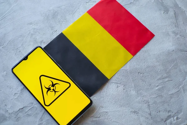 Epidemiologiska situationen i Belgien. Flagga och smartphone med nyheter och en symbol för biologisk fara. — Stockfoto
