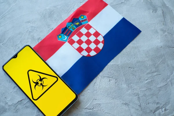 Situación epidemiológica en el país Croacia. Bandera y smartphone con noticias y símbolo de riesgo biológico . — Foto de Stock