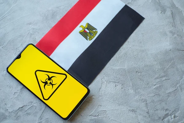 Situación epidemiológica en el país Egipto. Bandera y smartphone con noticias y símbolo de riesgo biológico . —  Fotos de Stock