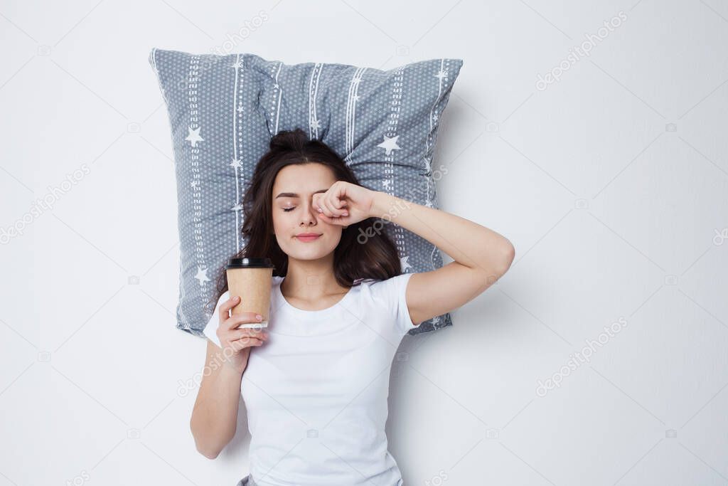 Good morning. Young woman drinking coffee with a pillow under her head,