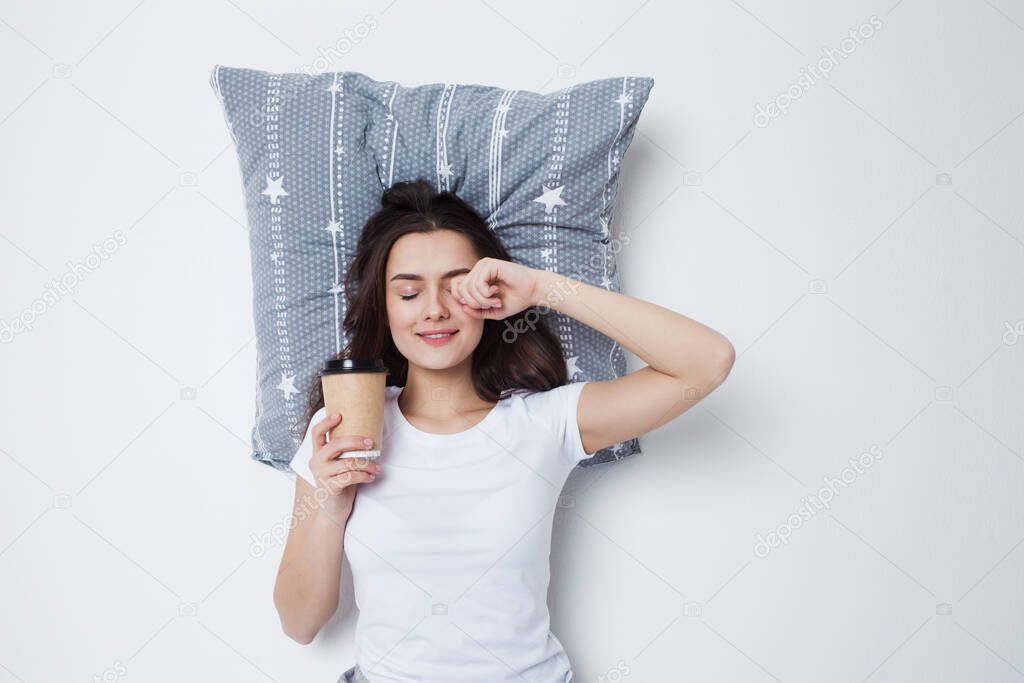 Good morning. Young woman drinking coffee with a pillow under her head,