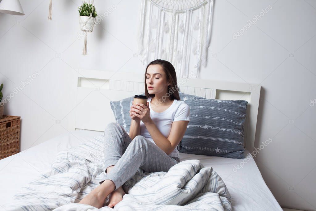 Wake up in bed in the morning and drink coffee. Young beautiful girl sitting on the bed