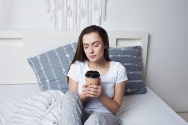 Sabah yataktan kalk ve kahveni iç. Genç güzel kız yatakta oturuyor.
