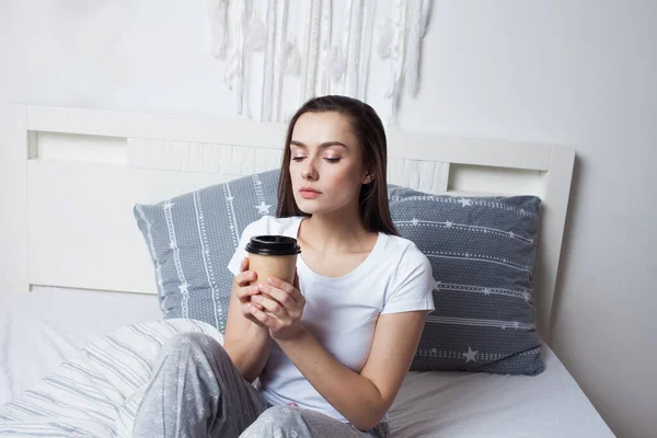 Wake up in bed in the morning and drink coffee. Young beautiful girl sitting on the bed