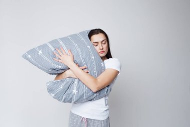 Uyku ve uykusuzluk, genç bir kadın yastığa sarılıyor ve ayakta uyuyor.