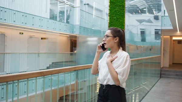 Phone conversation, a young emotional woman in a white shirt and glasses talking on a mobile phone