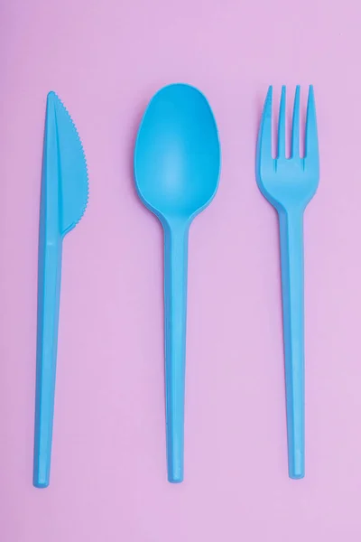 blue plastic cutlery set on pink background.